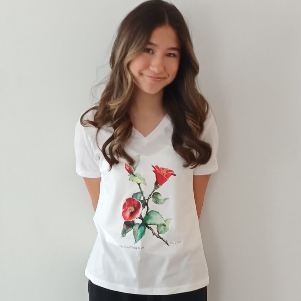 A girl with long, wavy hair wears a white v-neck t-shirt featuring a colorful flower design, standing against a plain background.
